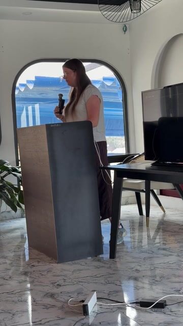 An elegant birthday celebration in Đà Lạt features a speaker presenting at a modern venue with stunning panoramic views of the city's iconic pine-covered mountains. The sophisticated indoor space showcases contemporary architecture, floor-to-ceiling windows, and polished interiors, capturing a memorable moment of celebration.